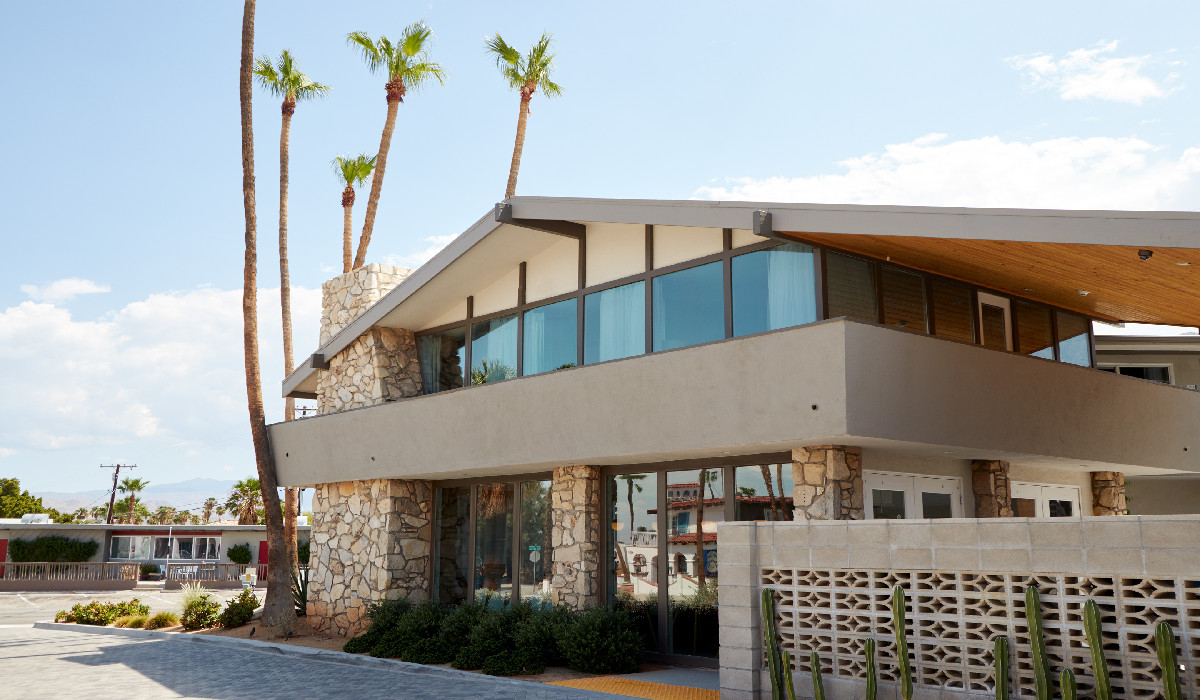 A modern building with stone and glass exterior, and palm trees in front.