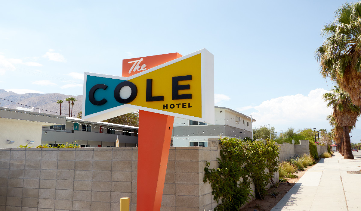 A colorful sign reading 'The Cole Hotel' in front of a building with a palm tree and mountain in the background.